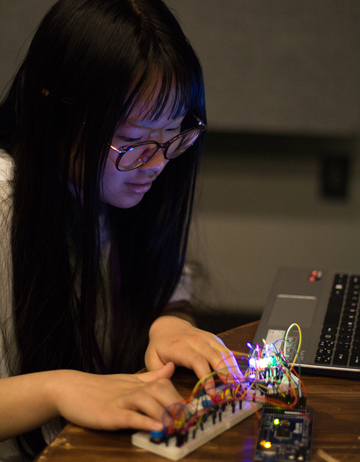 A single T9Hacks participant using their hands to test a physical computing project they built.